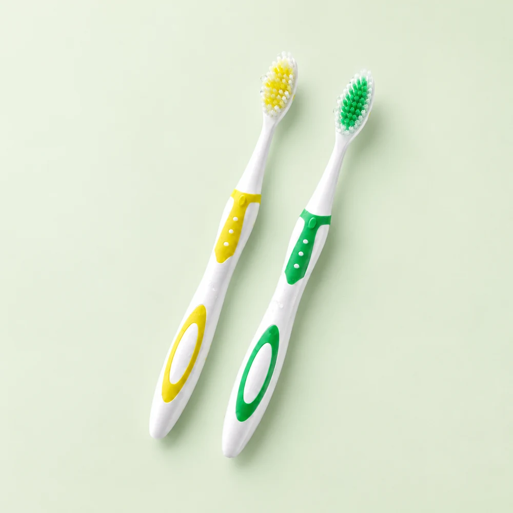 Two classic 5Doctors toothbrushes with yellow and green grips on a soft green background